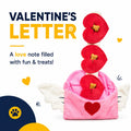 A Valentine's Day themed pet treat letter toy on a white background with promotional text. The toy features a pink winged envelope with a red heart on the front, three red heart-shaped envelopes stacked vertically, and a white letter inside.